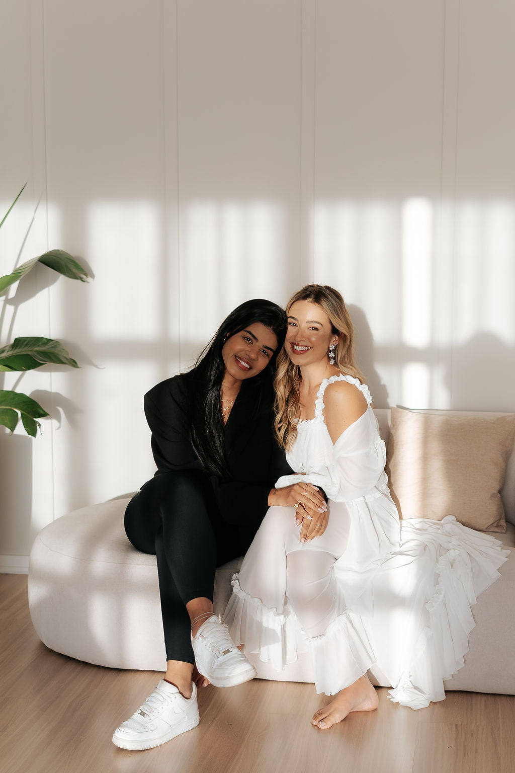 Duas amigas sorrindo abraçadas em um sofá